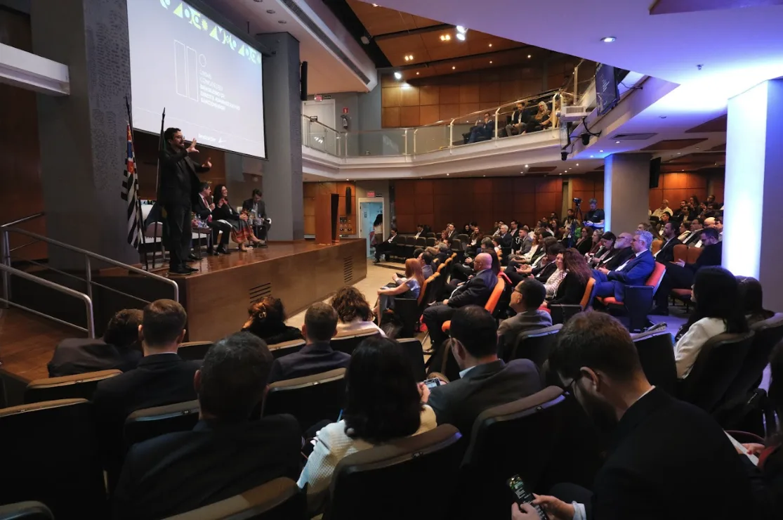 Auditório do congresso com plenária em andamento e público acompanhando o painel principal.